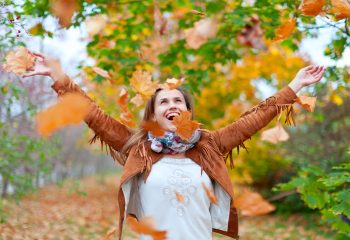 Happy woman throws autumn leaves in the park